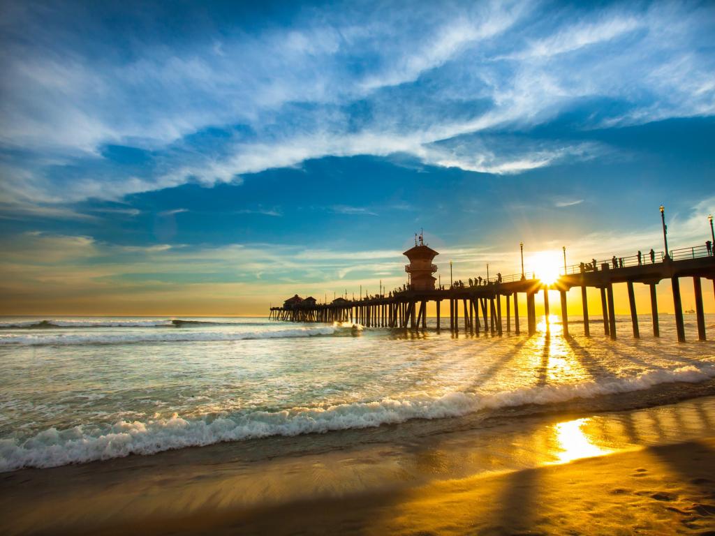 Huntington Beach Pier at sunset with soft waves lapping at the shore