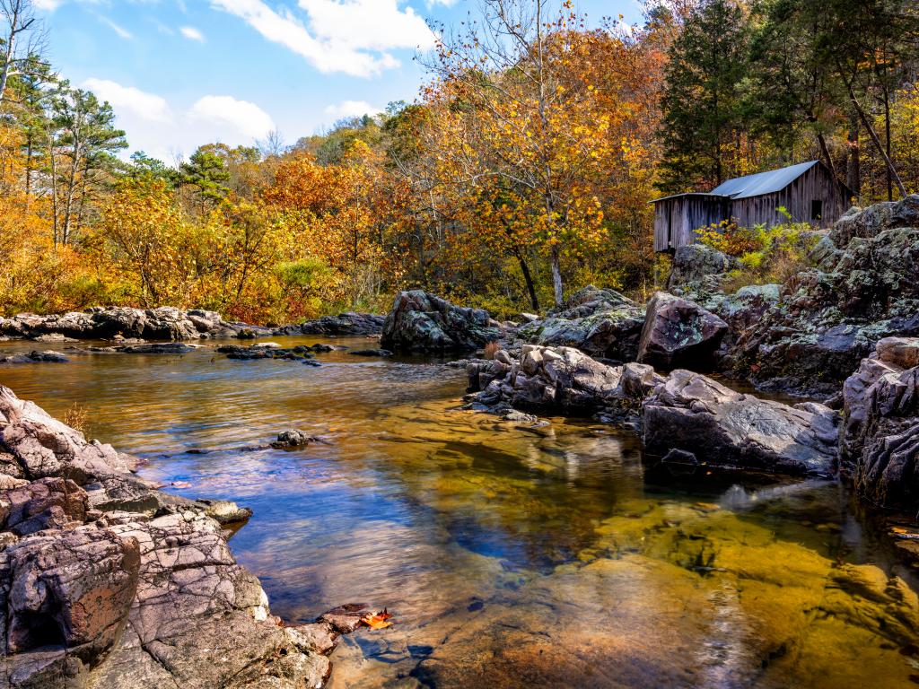 An abandoned wooden mill on the rocks next to a river in the Mark Twain National Forest in the fall.