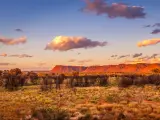 Watarrka National Park, Northern Territory, Australia taken at the George Gill Range in with grass and trees in the foreground and red hills in the distance at sunset.