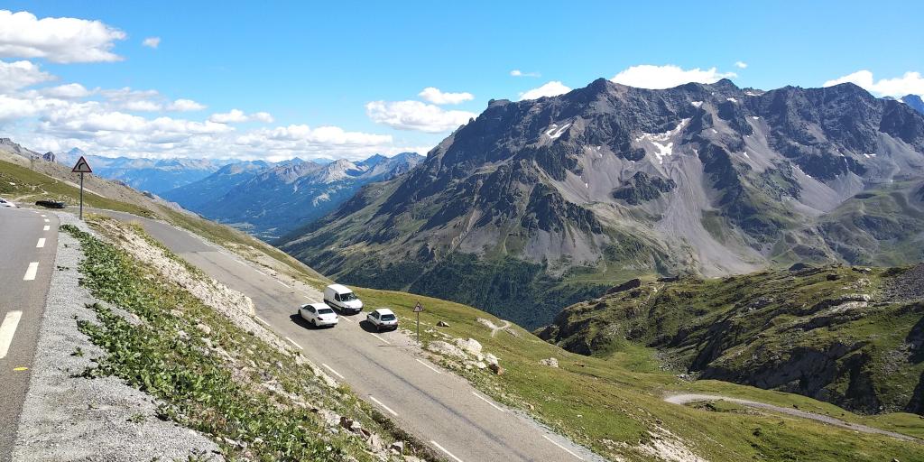 Cars parked on the side of the road on the Col de la Bonette, France with mountain peaks in the background 