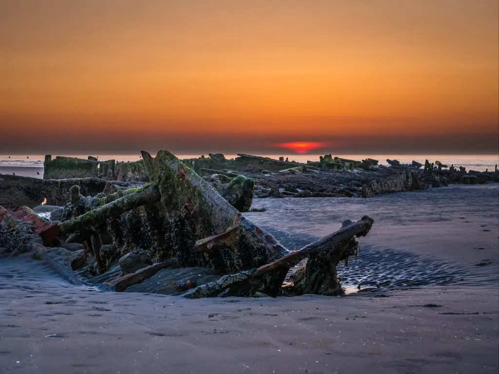Setting sun behind an exposed shipwreck at low tide from World War II at the beach