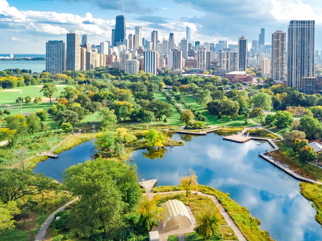 Chicago, Illinois, USA with a view of the skyline in the background and Lake Michigan in the foreground surrounded by lush greenery and trees.