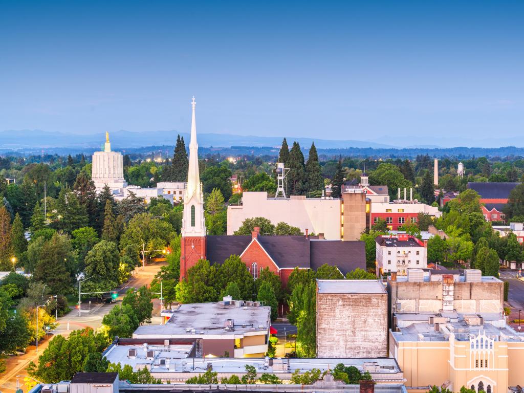 Salem, Oregon, USA with the downtown city skyline at dusk, street lights lit up and trees between the buildings. 