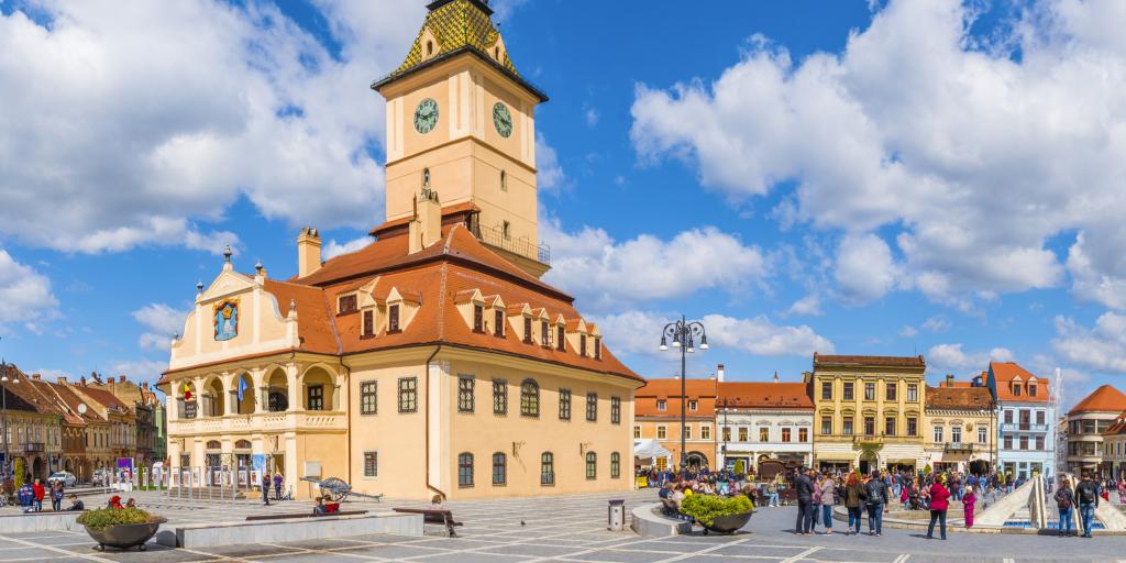 A view of the former council house surrounded by colourful buildings and people exploring in Council Square, Brasov 