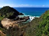 Port Macquarie, NSW, Australia looking down from the mountains to the beach below with a jagged shoreline above a blue sky.