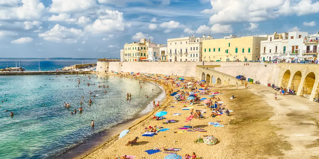People relaxing on Purity Beach with the town walls behind in Galipolli, Puglia 