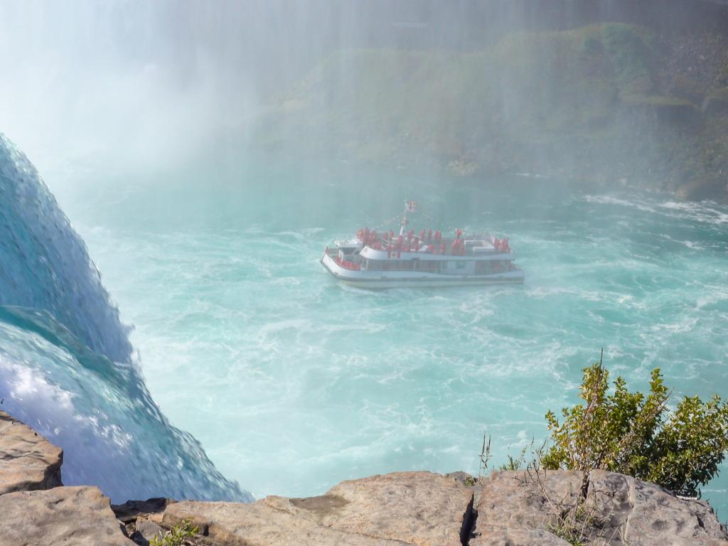 An amazing sight of a tour boat cruise with tourists enjoying the mists and witnessing the raging waterfall of Niagara Falls