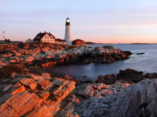 Panorama of Portland Head Lighthouse at dawn's first light, casting a warm glow on the rocks