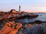 Panorama of Portland Head Lighthouse at dawn's first light, casting a warm glow on the rocks