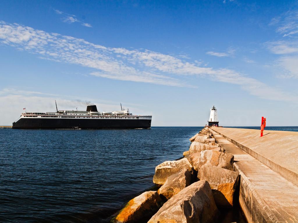 Large ship, the SS Badger car ferry coal-fired steamer, leaves port and passes by the North Breakwater Light in Ludington, Michigan.