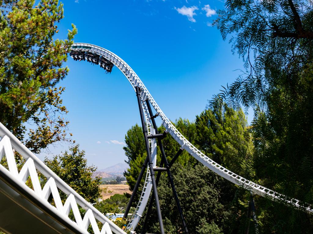 White roller coaster reaching up into blue sky with mountains in the distance