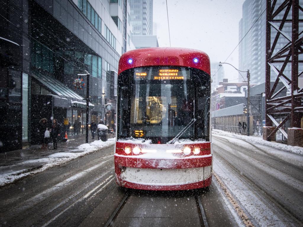 Bright red streetcar in the snow heading along the main roads in Toronto, Canada