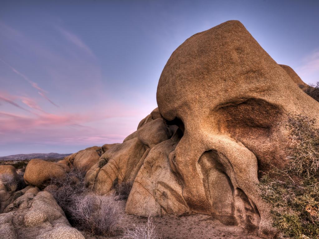 Imposing Skull Rock formation in Joshua Tree National Park, set against a purple and pink-hued sunset sky