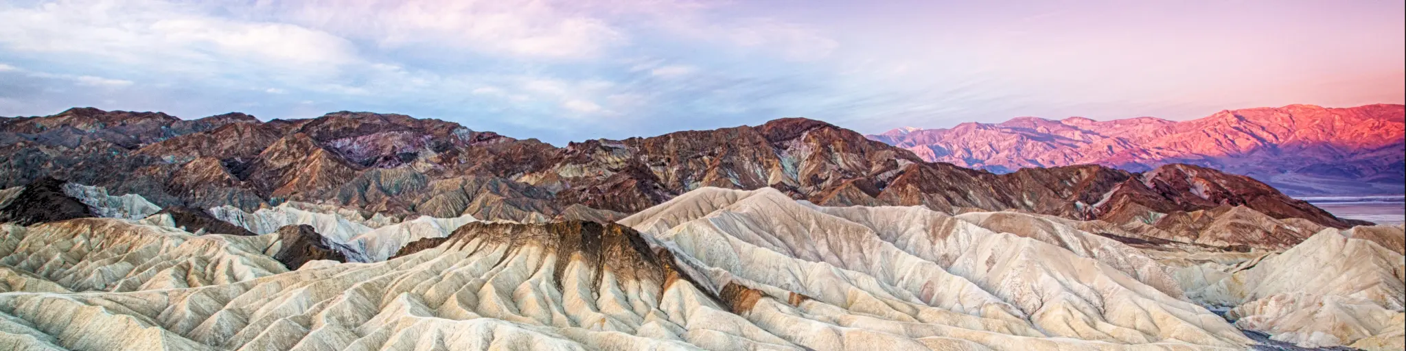 The sun rising over Zabriskie Point in Death Valley National Park, California with rugged rock formations and dunes in focus.