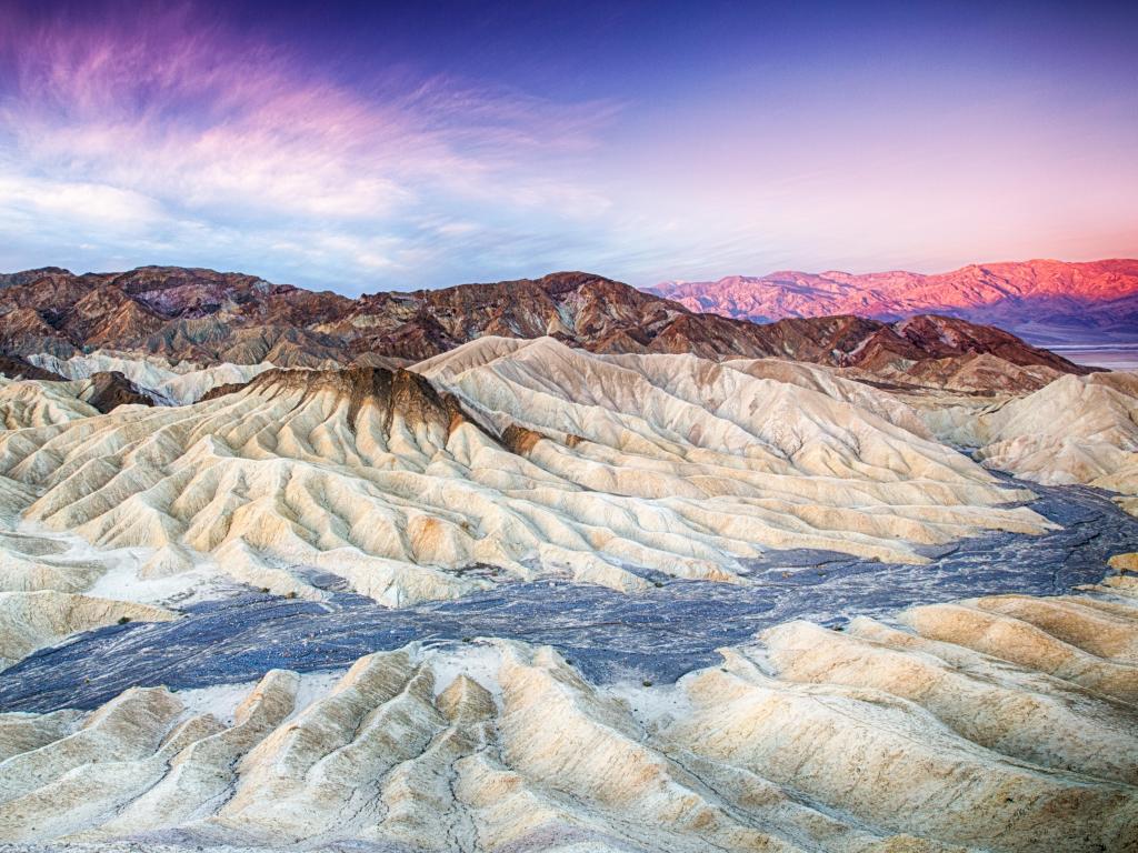 The sun rising over Zabriskie Point in Death Valley National Park, California with rugged rock formations and dunes in focus.