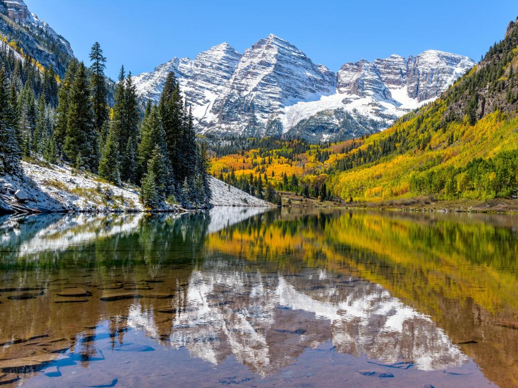 A wide-angle autumn midday view of snow coated Maroon Bells reflecting in crystal clear Maroon Lake, Colorado