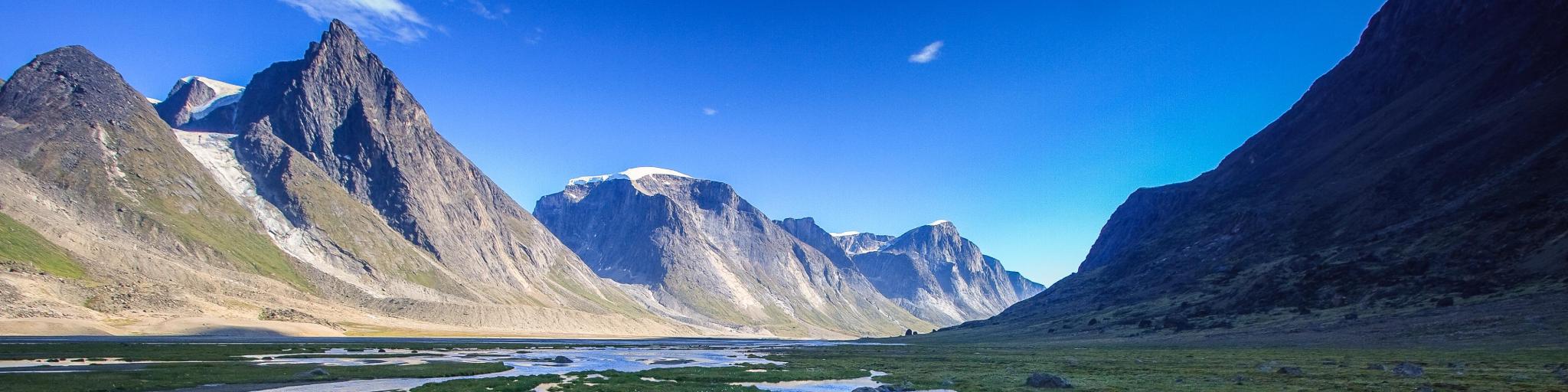 Panoramic view of the rugged Akshayuk Pass, Nunavut, Canada, with a blue sky above