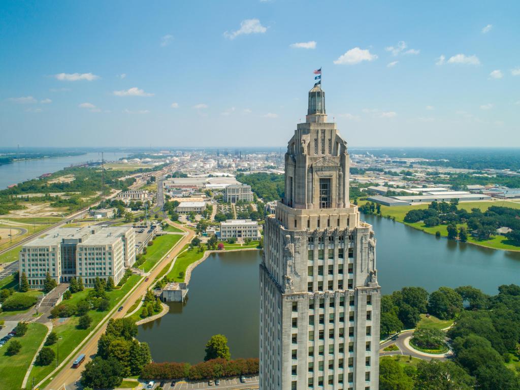 Baton Rouge, Louisiana, USA with an aerial closeup of the Louisiana State Capitol Building and welcome center overlooking the city and lake beyond.
