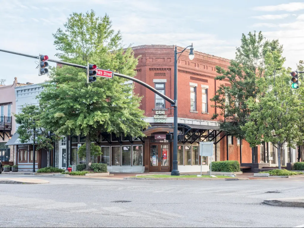 Historic red-brick buildings in downtown Tuscaloosa, Alabama on a summer's day. Green trees outside The Shirt Shop