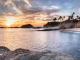 Rocks and sandy beach with sandy cliffs and palm trees
