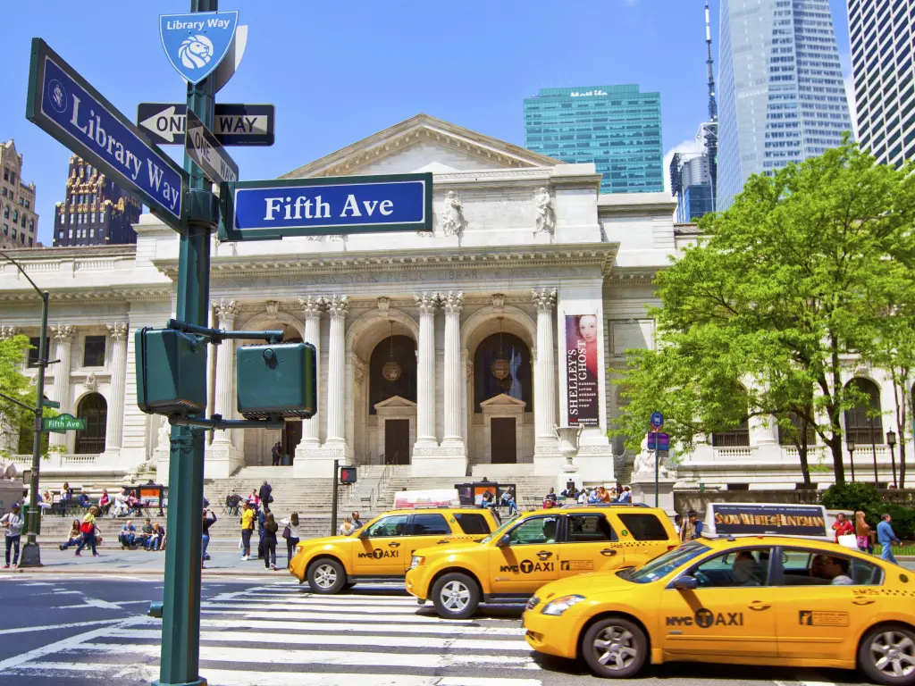  New York Public Library from the outside with 5th Avenue sign and yellow taxis