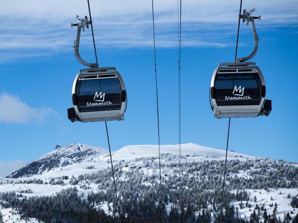 Two gondolas ascending a snowy slope on a sunny day