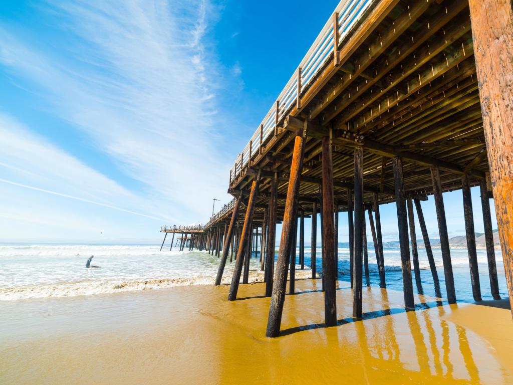 Pismo Beach pier, California, USA with a surfer in the sea and the boardwalk in the foreground.