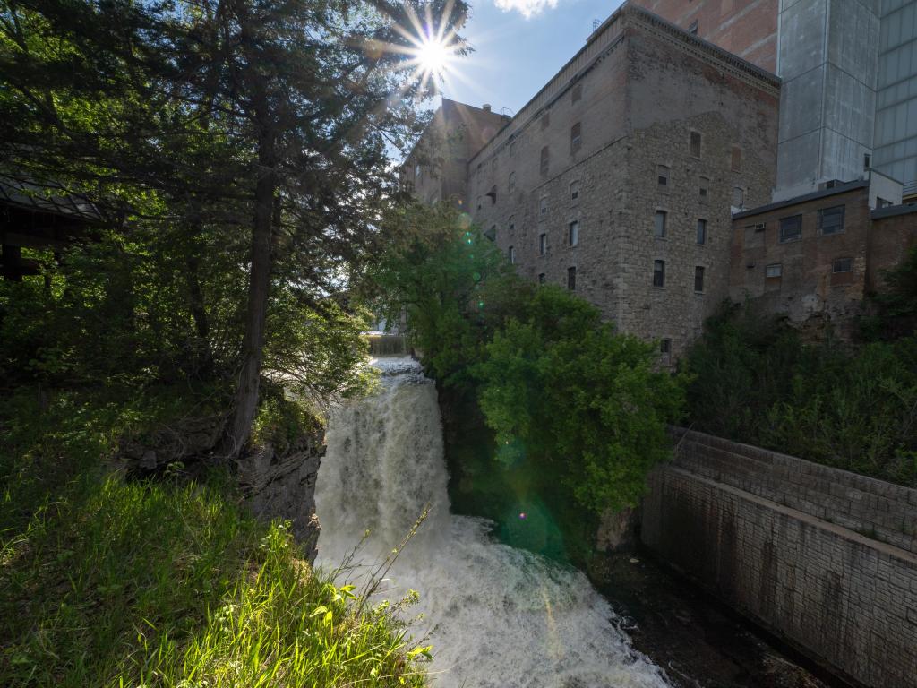 Vermillion Falls, Hastings, Minnesota, USA taken at the site of an urban waterfall next to an old factory on a sunny day with trees surrounding. 