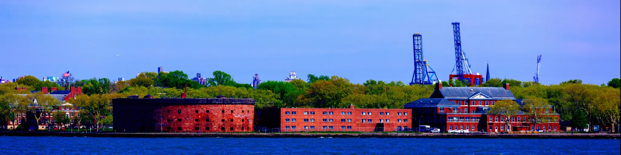 A worm's eye view of Castle Williams of General Island from New York Harbor with trees green trees and tower in the back on a sunny day