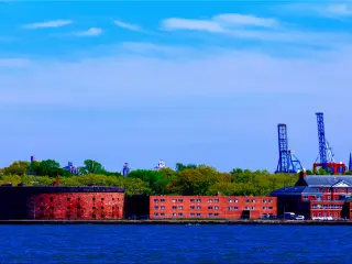 A worm's eye view of Castle Williams of General Island from New York Harbor with trees green trees and tower in the back on a sunny day