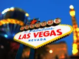 Las Vegas sign lit up at night with the replica of Eiffel Tower and a replica hot air balloon in the background