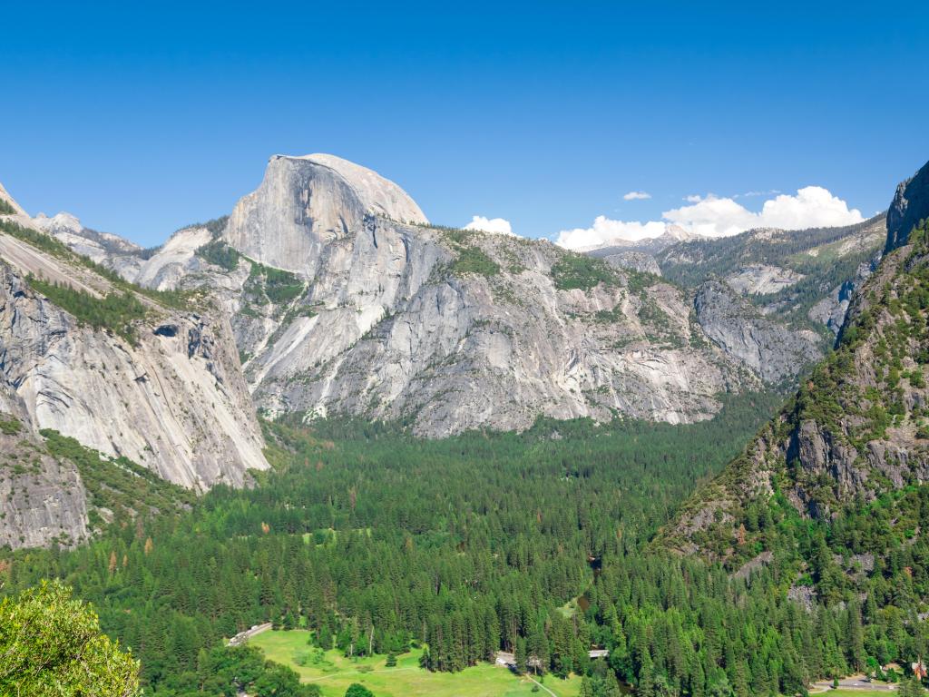 View of Half Dome and forested valley below from a height, sunny weather with blue skies