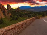 A dark red and yellow sunset and a foreboding sky hangs over a walled road at Garden of the Gods in Colorado