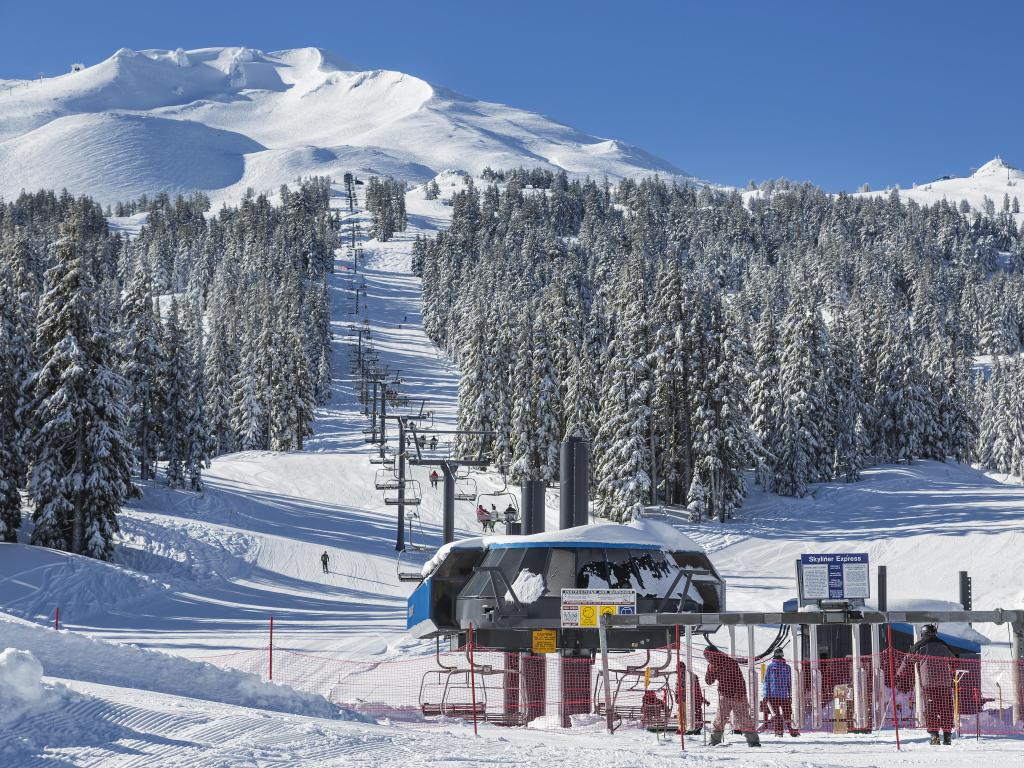 Chair lifts at the bottom of the mountain, snow covered, forested hills in the beackground