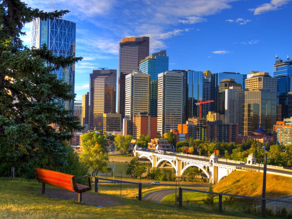 Calgary, Alberta, Canada Park with a red bench overlooking skyscrapers of Calgary, against a blue sky.