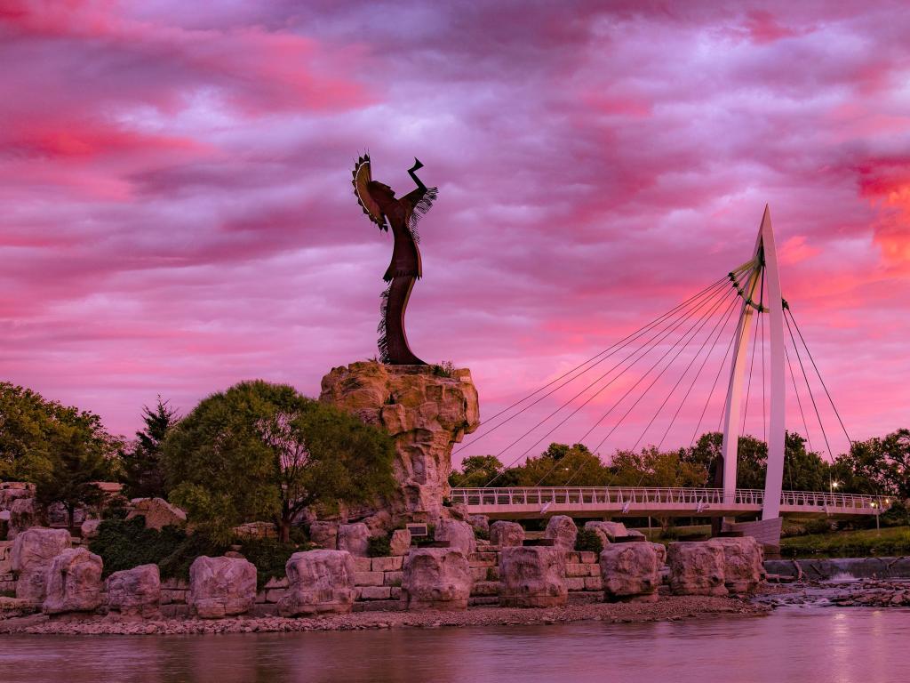Keeper of the Plains statue overlooks Wichita at sunset, with a pink and purple hued sky above