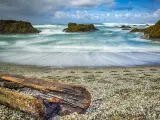View of frothing blue waters, with colored glass shoreline and rocks dotted across the coast