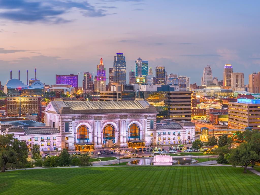 Kansas City, Missouri, USA taken of the downtown skyline with Union Station at dusk, a green grass area in the foreground. 