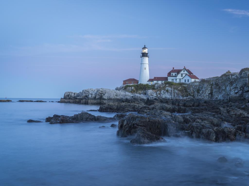 Casco Bay, Maine with the historic lighthouse on top of the cliffs, with the sea below and a few buildings nestled by.