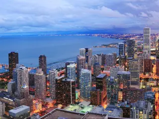 high rise buildings in sunset light showing in pinks and blues with lights shining, lake in background
