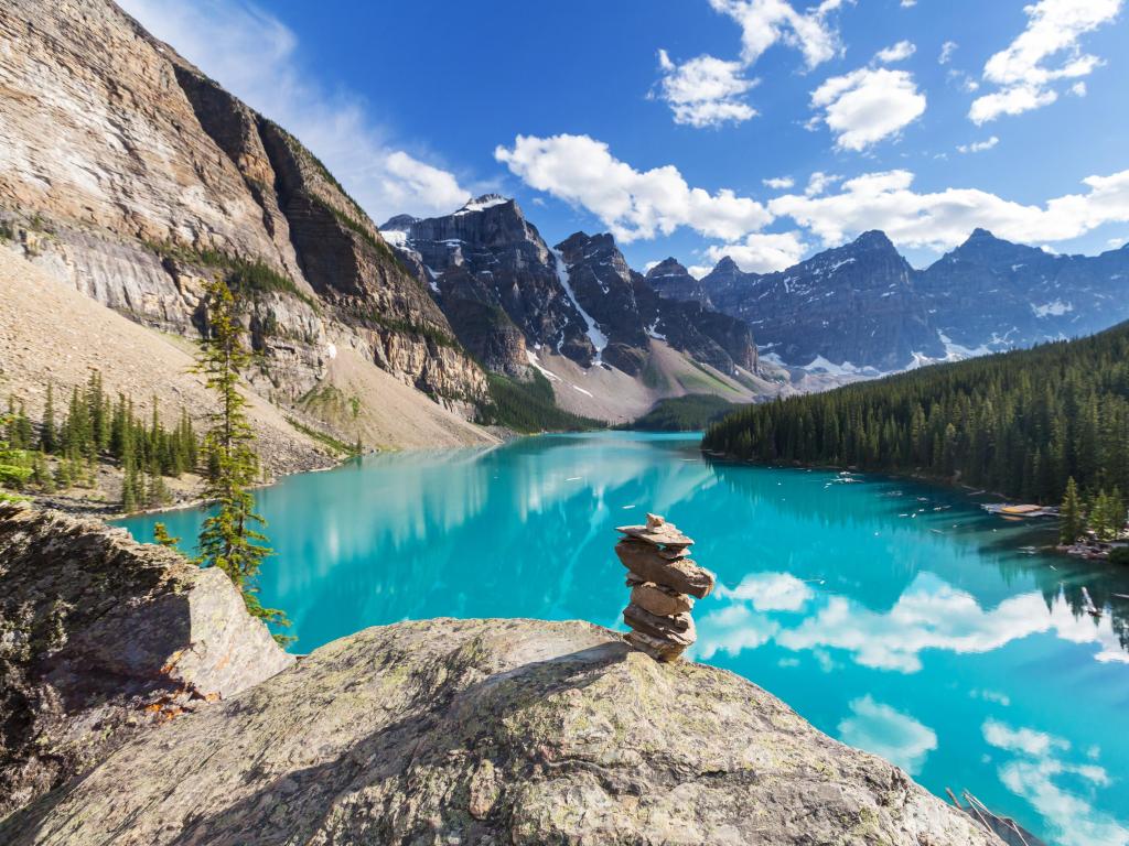 Banff National park, Canada taken at beautiful Moraine Lake with rocks in the foreground and the turquoise water reflecting the snow-capped mountains in the distance on a sunny day.