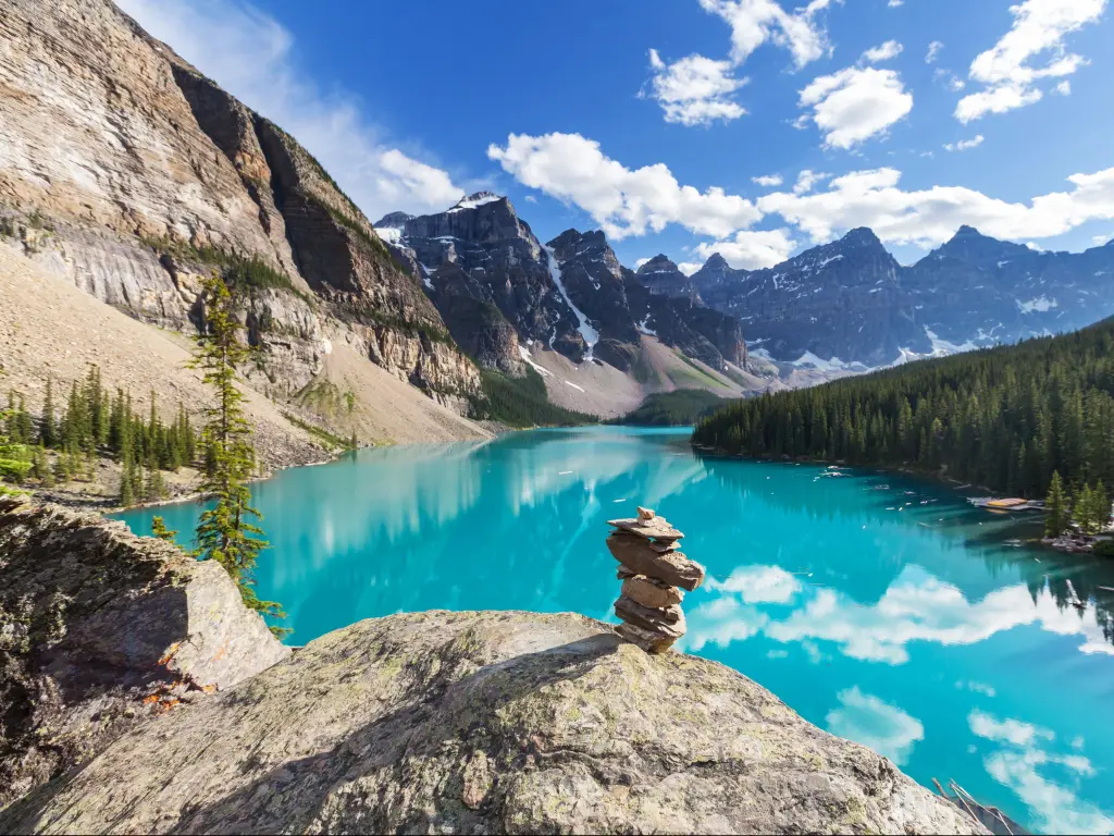 Banff National park, Canada taken at beautiful Moraine Lake with rocks in the foreground and the turquoise water reflecting the snow-capped mountains in the distance on a sunny day.
