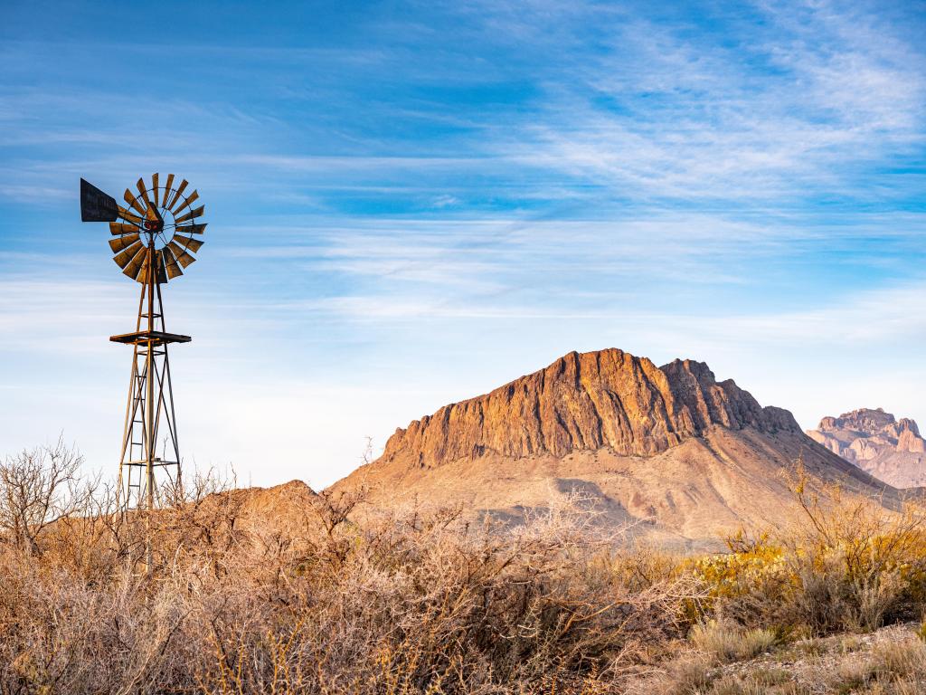 A small windmill in the foreground with a Texas desert landscape and blue skies