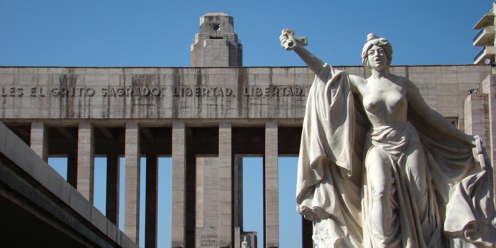 A close up of a female statue raising her arm at Monumento a la Bandera, Rosario, Argentina, with the columns of monument in the background
