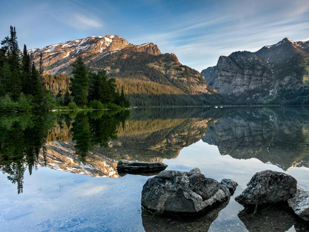 Phelps Lake, North Carolina, USA taken during a tranquil morning with mountains in the distance, rocks in the foreground and the lake reflecting the trees.