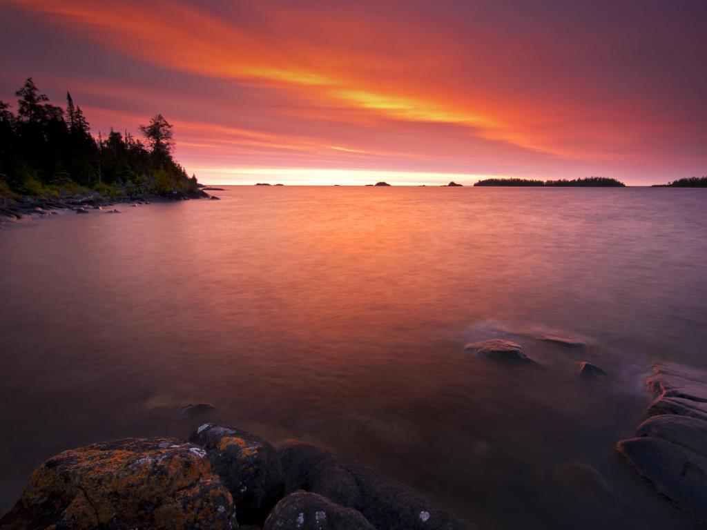 Isle Royale National Park, Michigan taken at Rock Harbor at sunrise with the sky reflecting off the water in the foreground. 