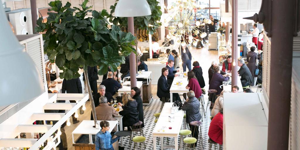 People sit inside drinking beers and eating food in the Mercado Lonja del Barranco in Seville