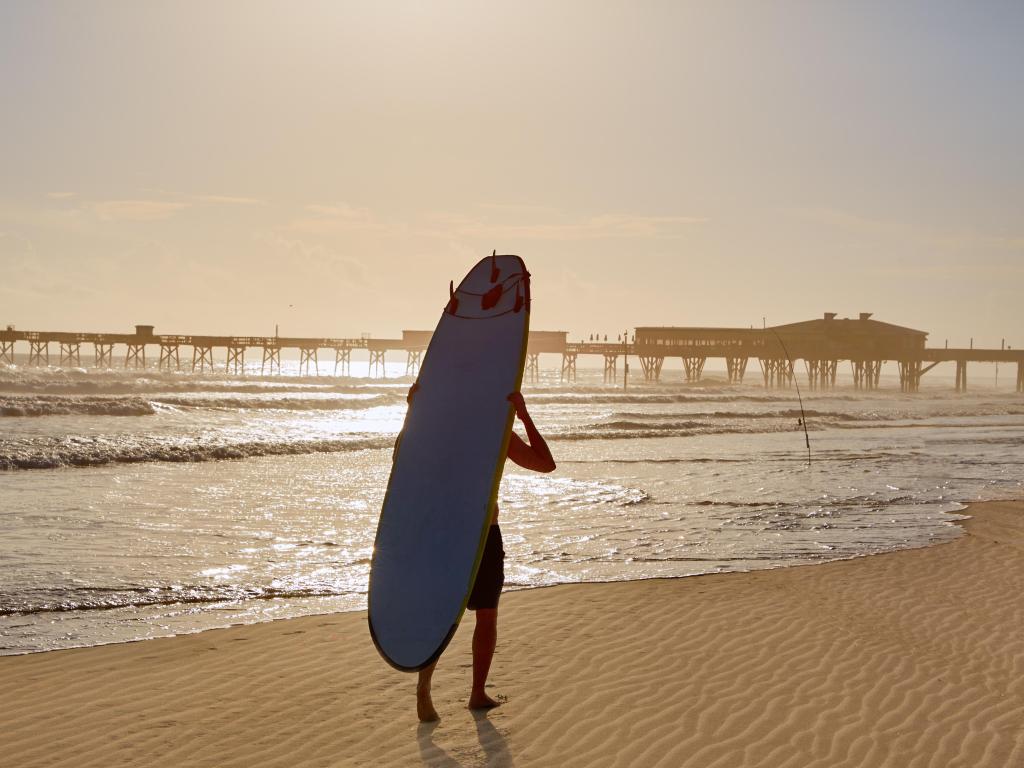 Daytona Beach in Florida shore with pier and unknown surfer walking USA