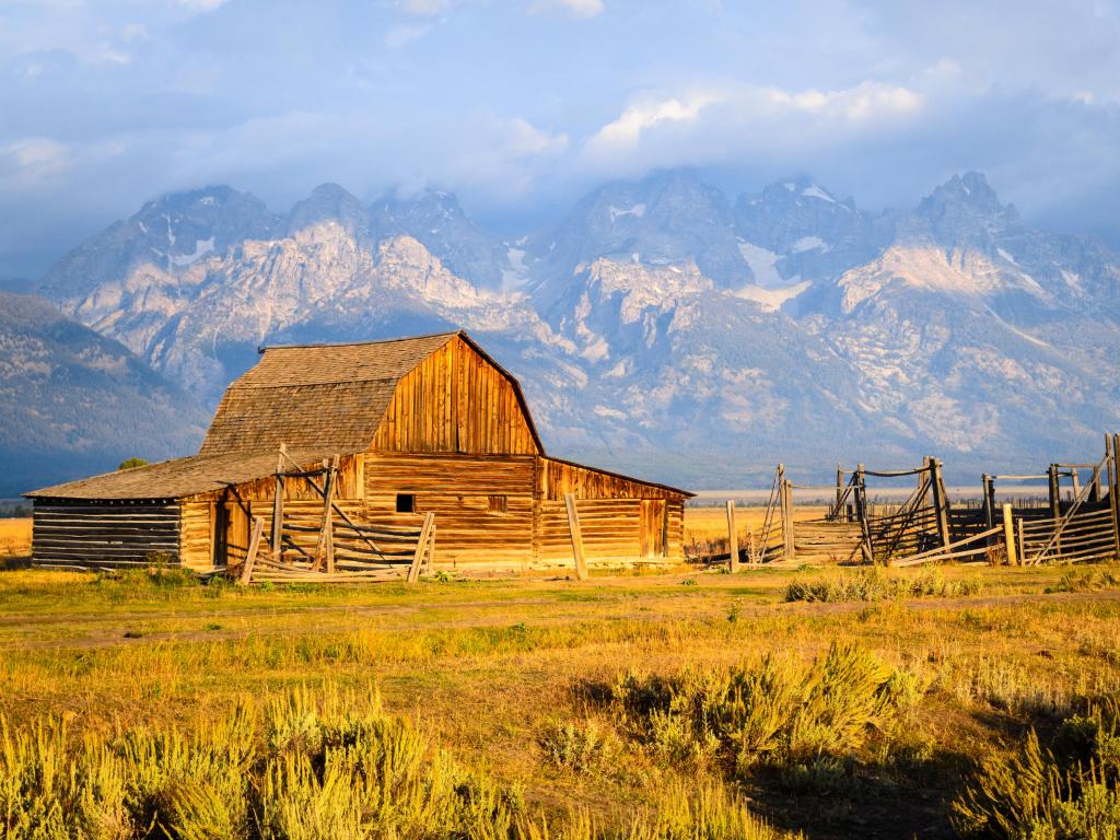 Wooden barn lit up in golden light on flat farmland with mountains behind