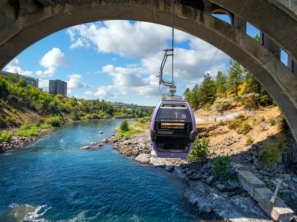 A purple cable car gondola descends under a bridge, giving a beautiful view of the river from Spokane's SkyRide attraction